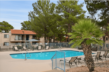 A pool surrounded by chairs and trees with a building behind it.
